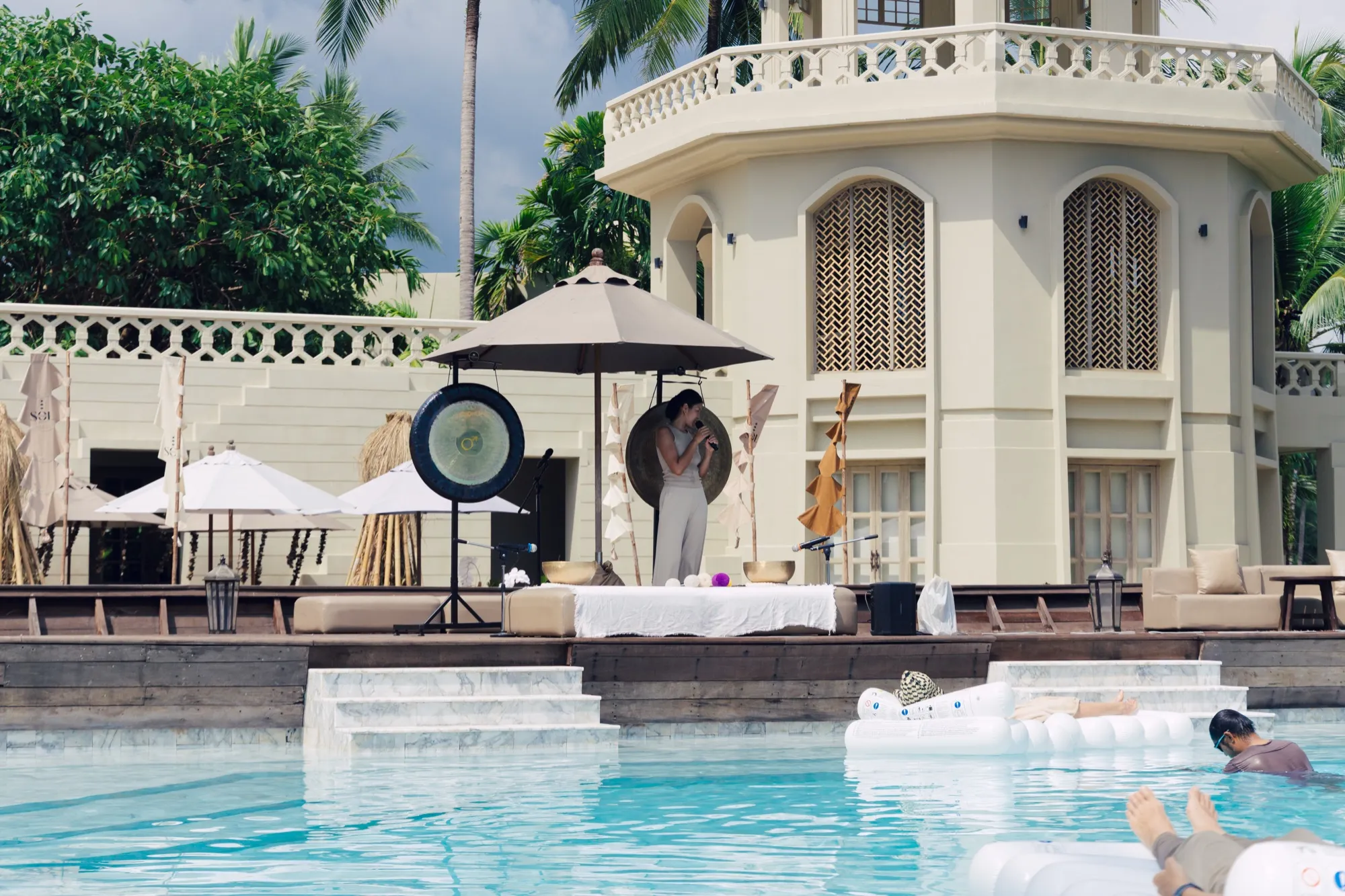 Ice performing poolside at a resort event, guests floating on the water in front of her.