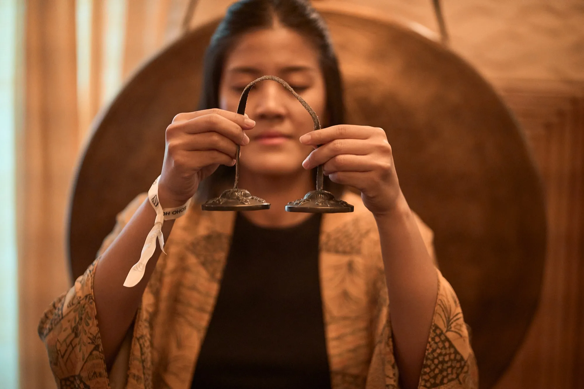 Ice holding tingsha cymbals in front of a gong, eyes closed.