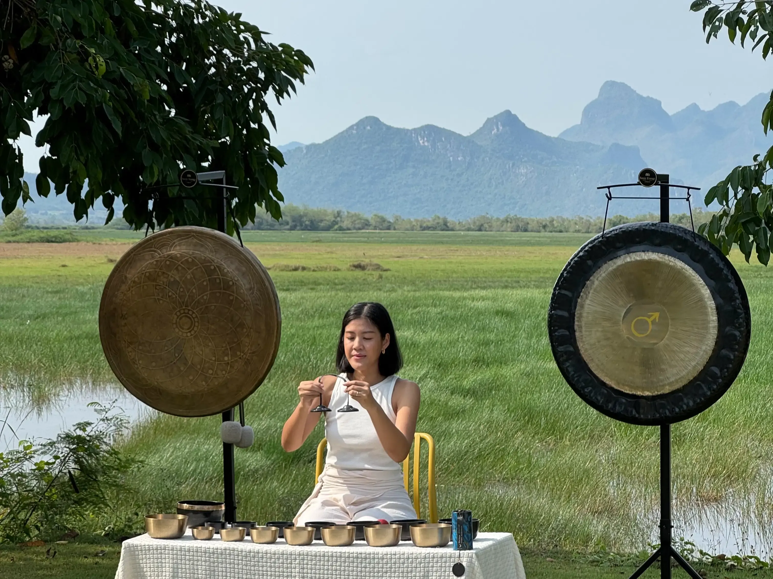Ice playing tingsha cymbals with a mountain view behind.